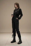 Woman wearing a black outfit with zippers and chains in an indoor setting.